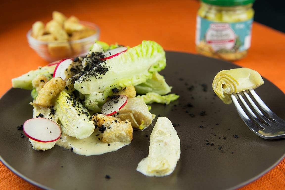Ensalada césar con cogollos de lechuga, alcachofas marinadas, láminas de rábano y polvo de aceitunas negras